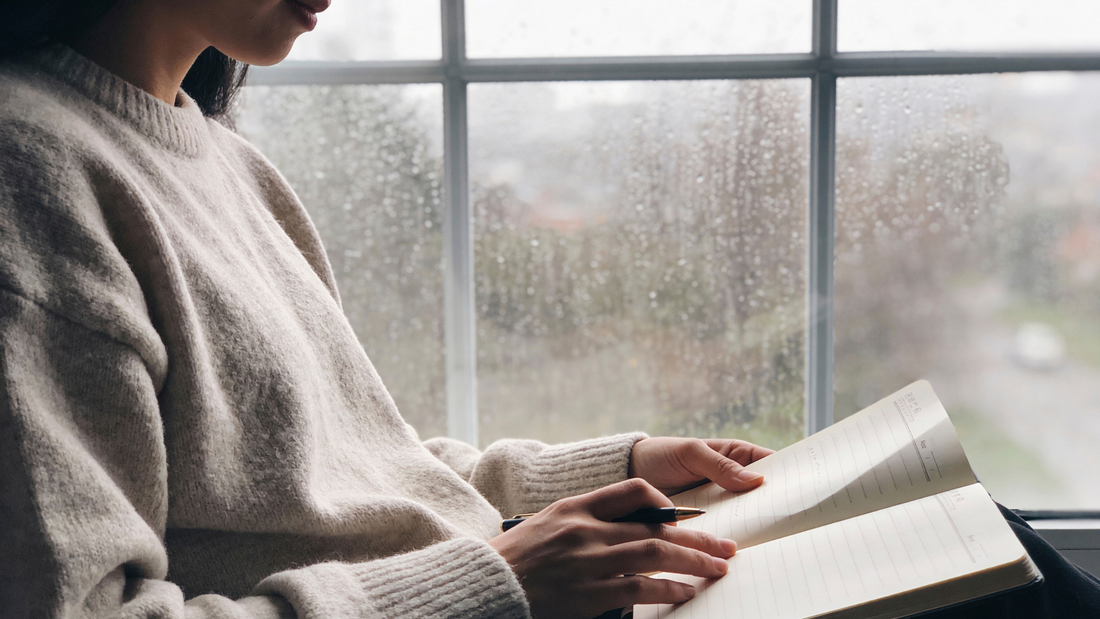 person journaling by a window in soft natural light, representing calm reflection, stress relief, and supporting skin health from within 