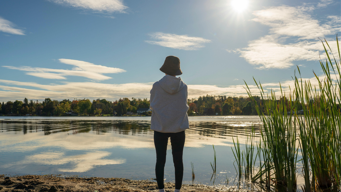 Person standing by a calm lake in natural light, reflecting a holistic lifestyle that supports skin health